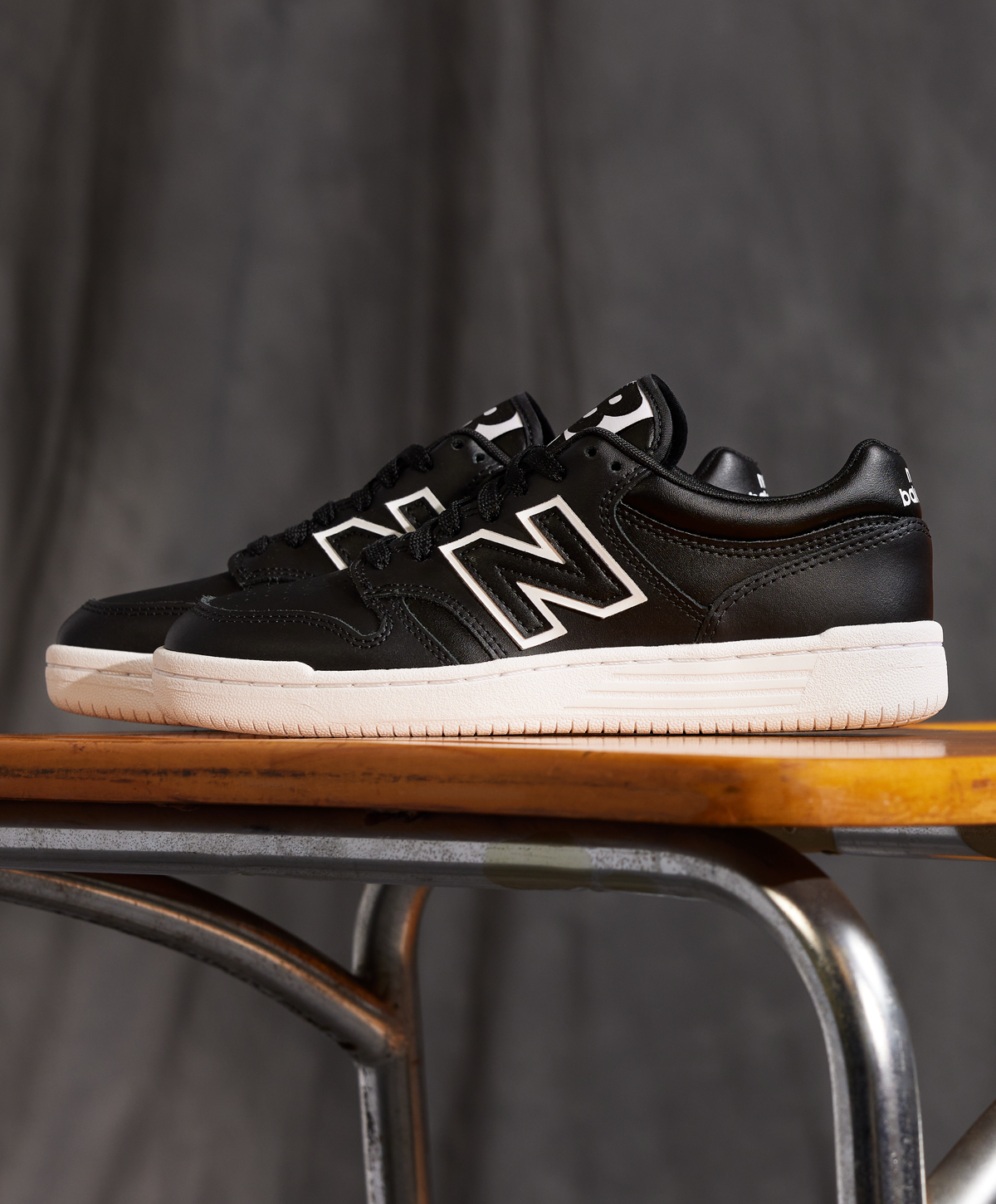 Sort sneaker med hvid sål og hvidt "N" logo, placeret på en træbænk med metalben.