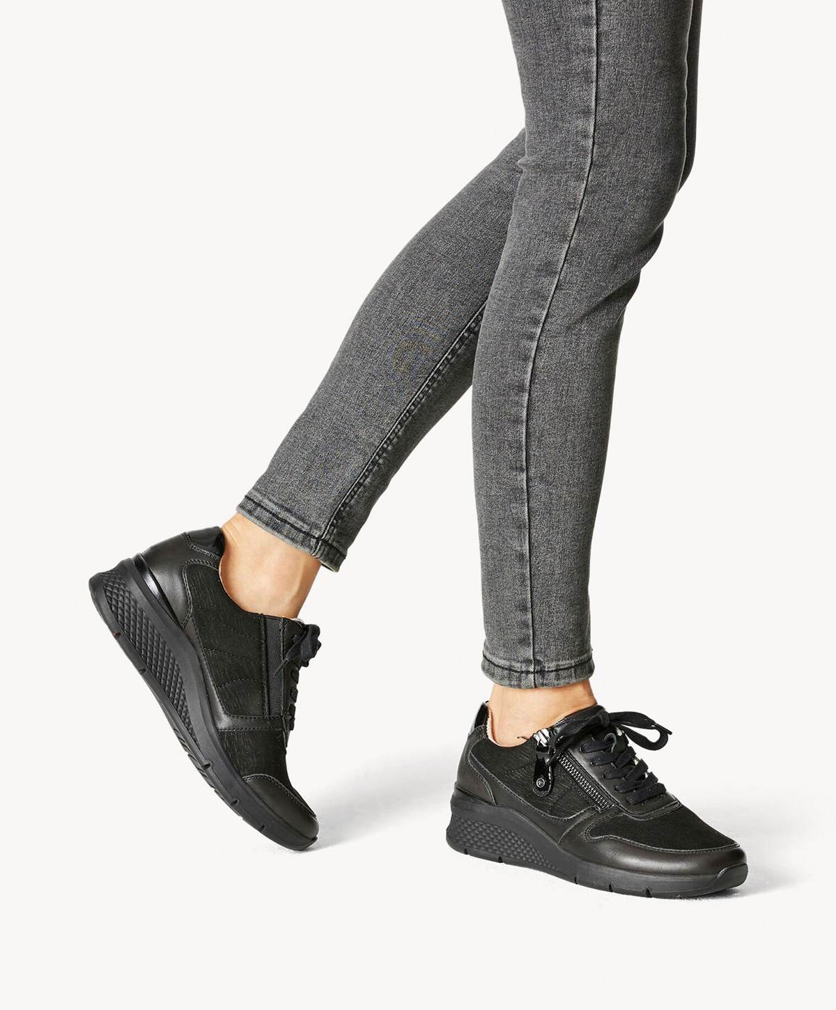 Sort sneakers på en person iført grå jeans.