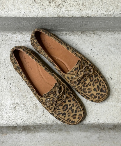 Et par loafers med leopardmønster placeret på en grå betonoverflade.