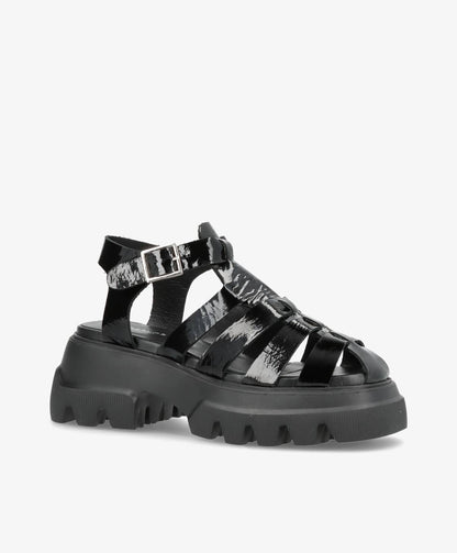 Sort sandal med tyk, rillet sål og justerbar rem med spænde.