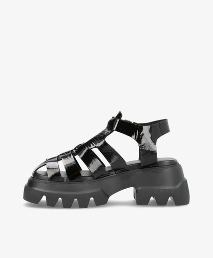 Sort sandal med tyk sål og remme i skinnende materiale.