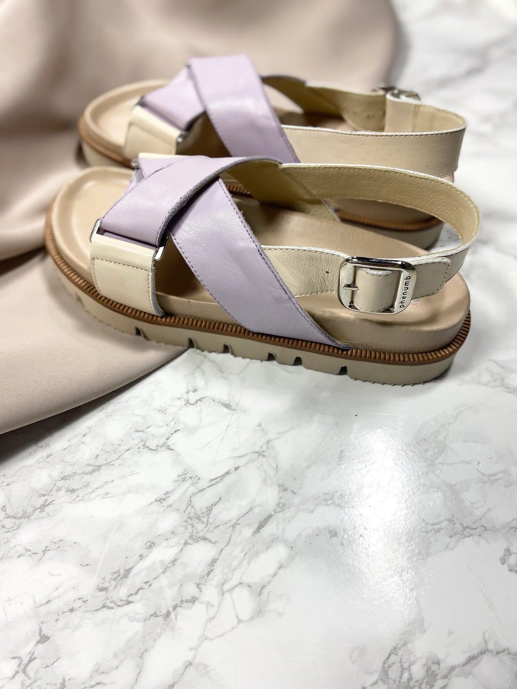 Beige og lilla sandaler med spænder på en marmoreret overflade.